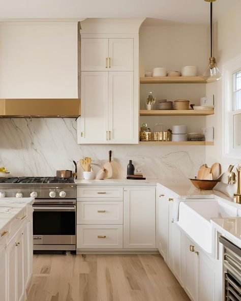 Happy Monday!! ✨✨✨ This kitchen exudes a timeless and muted elegance. The cabinetry is off-white, paired beautifully with light wood flooring, creating a serene and inviting atmosphere. The countertops and backsplash are made of quartz, adding a touch of luxury. Open shelving displays neatly arranged dishes and kitchenware, enhancing the minimalist aesthetic. The gas stove and gold-coloured accents, such as the cabinet handles and pendant light fixture, add both functionality and style to th... White And Wood Kitchen Brass Hardware, White Wood And Gold Kitchen, White Gold And Wood Kitchen, Kitchen Design White And Gold, Warm White Cabinets Kitchen, Kitchen Gold Fixtures, White Kitchen Cabinets With Gold Handles, Kitchen Cabinets With Gold Handles, Off White Kitchen Cabinets With Quartz