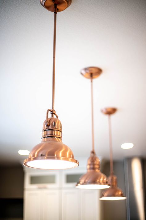 Copper metal hanging light fixtures over a huge kitchen island with matching copper hardware. Modernize your farmhouse design with a combination of gray/blue cabinets and white cabinets. Paired with dark hardwood floors and a rustic brick fireplace and a large solid wood mantel Modern Farmhouse Kitchen Light Fixtures, Farmhouse Fixtures, Kitchen Cabinets Light Wood, Copper Kitchen Island, Huge Kitchen Island, Farmhouse Kitchen Light Fixtures, Kitchen Light Fixtures, Copper Light Fixture, Solid Wood Kitchen Cabinets