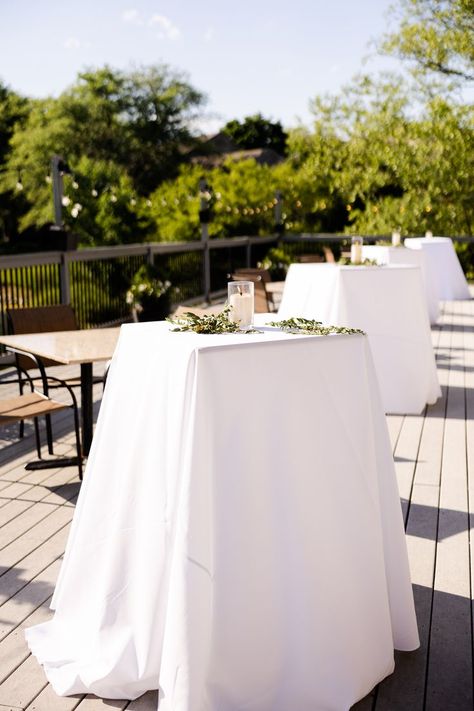 This image features a wedding cocktail hour outside on a patio. The cocktail tables have a white linen, accented with one pillar candle and some hand laid greenery. Table Greenery, Table Candles, Photography Location, Single Candle, Candle Table, Location Photography, Cocktail Table, Pillar Candle, Cocktail Hour