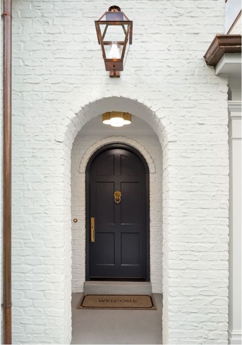 A white painted brick Tudor house with arched doorways, black front door, and copper downspouts. White Painted Brick Exterior, Arched Front Door, Painted Brick Exteriors, Timeless Interior Design, Brick Arch, Black Front Doors, Timeless Interior, Tudor Style Homes, Brick Exterior House