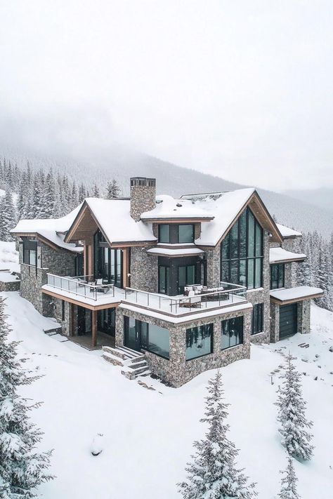 Aerial view of a snowed in modern mountain mansion with modern stone foundation with large porches and multi pitched second floor roof large windows. Indulge in luxurious mountain mansions that seamlessly blend natural beauty with luxurious living, offering a unique retreat away from the everyday hustle. Home In The Mountains Aesthetic, Modern Cabin Mansion, Chalet Mansion, Fancy Modern House, Mansion In Snow, Modern Mountain Mansion, House In Mountains Dream Homes, House In Snowy Mountains, Large Modern Mansion