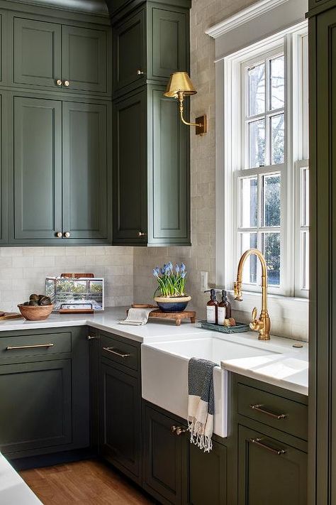 Kitchen features forest green cabinets with nickel pulls and an apron sink with an antique brass vintage gooseneck faucet under a window, lit by a brass sconce on marble subway tiles. Forest Green Cabinets, Forest Green Kitchen Cabinets, Kitchen Sink Window, Best Kitchen Faucets, Best Kitchen Sinks, Gold Faucet, Apron Sink, Brass Kitchen Faucet, Green Kitchen Cabinets