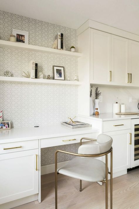 A separate office wasn’t in the works for the homeowners, but they found a solution: a kitchen desk niche. It’s just right off the main kitchen area and matches with the rest of the white cabinetry. Bold, patterned wallpaper gives the desk a sense of separation from the rest of the kitchen, too. Desk On Kitchen Counter, Home Office Near Kitchen, Kitchen Computer Desk, Home Office Off Kitchen, Office Space In Kitchen Area, Office Desk In Kitchen, Built In Desk With Wallpaper, Kitchen Nook Office Ideas, Kitchen With Built In Desk