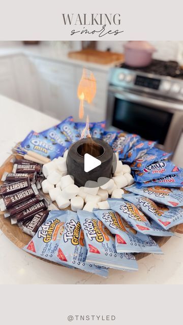 Tara Tedesco | Tnstyled on Instagram: "WALKING S’MORES BOARD!   Comment SMORES and I’ll send you my mini fire pit! It also comes with cute little sticks to roast marshmallows. If you guys have seen the “walking” tacos this is a take on that that I have seen a few times! Had to try it out and I can confirm it’s such a fun idea!   I added a bunch of cookies, chocolate and marshmallows to a board along with the mini firepit. You can change this up and use different candy and cookies!   #summerideas #summertime #smores #camping #vacation" Walking Smores In A Bag, Smores Charcuterie Board Ideas, Walking Smores, S’mores Board, S’mores Bar, Smores Charcuterie Board, Goonies Halloween, Smores Table, Smores Ideas