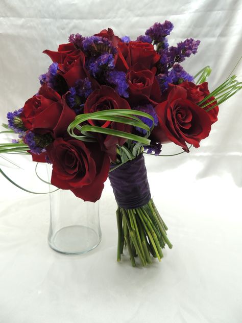 Bridal bouquet made of red roses and purple statice, with bear grass loops for an extra beautiful look. Red Roses And Lavender Bouquet, Red And Purple Rose Bouquet, Black Red And Purple Bouquet, Dark Color Wedding Bouquet, Lavender Red Wedding, Red And Purple Bouquet Wedding, Red Purple Bouquet, Dark Purple And Red Wedding Theme, Purple And Red Wedding Flowers