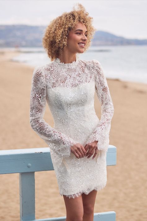 Embrace the enchantment created by this sparkly short wedding dress that’s designed to make you fall in love with her the moment you try her.Simone’s high neck and long lace sleeves not only offer some modesty, they offer vintage elegance and her shimmering sequins throughout add a touch of modern glam.Her open keyhole back creates a dramatic contrast, ensuring you look stunning from every angle.Perfect for a beach wedding or intimate elopement, this dress combines comfort and style effortlessly Short Wedding Dress With Sleeves, Wedding Dress With High Neck, Long Lace Sleeves, Wedding Dress With Sleeves, Dress With High Neck, Sparkly Shorts, Mini Wedding Dresses, Intimate Elopement, Wedding Reception Dress