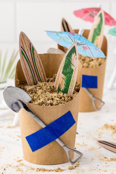 A beach themed sand pudding dessert with surf boards and paper umbrella. Sand Bucket Dessert, Pool Party Favours, Sand Pudding Cups, Sand Pudding Dessert, Surf Board Cake, Totally Twobular, Sand Dessert, Sand Pudding, Pudding Cup Recipes