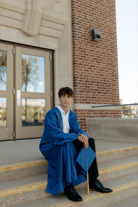 Male in blue gown holding graduation cap on steps of school. Cool Graduation Pictures For Guys, Cap And Gown Senior Pictures For Guys High Schools, Guy Cap And Gown Pictures, Male Cap And Gown Pictures, Boy Cap And Gown Pictures, Cap And Gown Senior Pictures For Guys, Guys Graduation Pictures, Guy Graduation Pictures, Graduation Poses For Guys