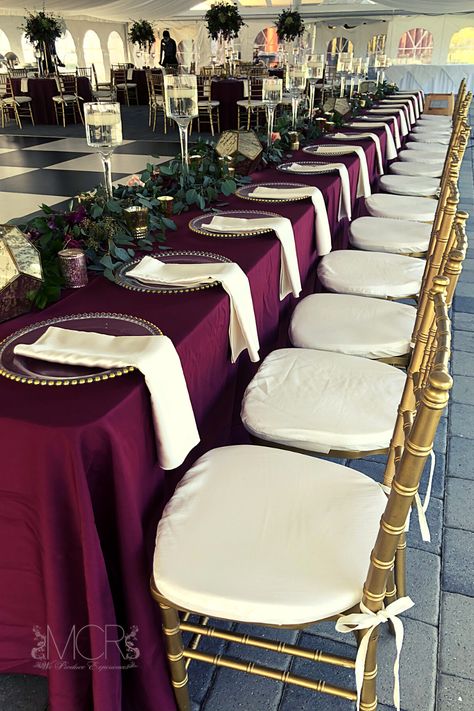 An elegant art deco themed wedding with burgundy linens and gold accents. An abundance of greenery lines the long head table, floating candles in wine glass vases and gold geometric lanters add both vintage and modern elements to the wedding decorations. Gold chiavari chairs with ivory cushions and napkins brighten the decor and match the black and white checkered dance floor. #dream #dreamwedding #centerpieces #reception #weddingreception #dancefloor #october #octobercolors Wedding Decorations Gold, Art Deco Themed Wedding, Head Table Design, Checkered Dance Floor, Art Deco Wedding Theme, Gold Chiavari Chairs, Chiavari Chairs, Modern Elements, Head Table