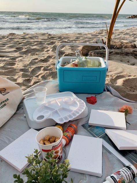 Beach picnic, with painting materials as canvas, paint, brushes, ice chest with cold drinks, and flowers Painting On Beach Picnic, Beach Picnic Painting, Beach Paint And Sip, Painting On The Beach Date, Paiting Aesthetic Date, Picnic Beach Ideas, Picnic Painting Ideas, Beach Date Ideas, Beach Picnic Ideas