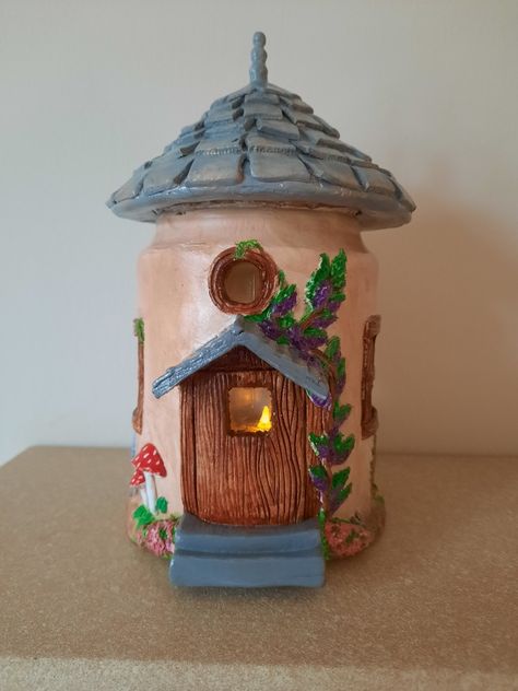 A fairy house made from a recycled pickle jar and air dry clay. The house is hand painted using acrylics and is lit using battery operated string lights. Jar Fairy House, Clay Tree, Recycled Jars, Battery Operated String Lights, Pickle Jar, Pickle Jars, Fairy House, Spice Jars, House Made