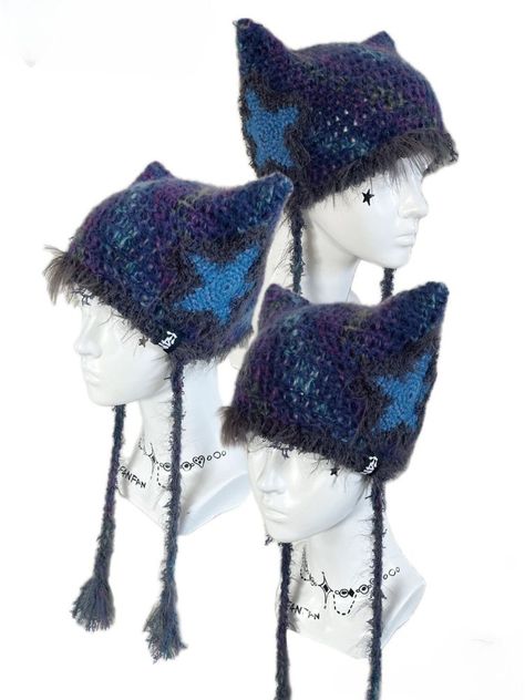 Featuring adorable cat ear shapes adorned with star motifs, this beanie is perfect for keeping you snug and on-trend. Complete with two long tails for added flair, it's the perfect accessory to elevate your winter wardrobe. Embrace the magic of the season with this enchanting addition to your wardrobe, where every wear promises a delightful touch of playful elegance. Hand knit over the course of 4 hours. Polyester & 10% Wool Washing Instructions:Can be washed in low-temperature water and ironed Cute Winter Accessories, Alt Crochet Ideas, Cat Beanies, Cat Crochet Beanie, Cool Crochet Hats, Cat Ear Hat, Cat Ears Beanie, Crochet Winter Clothes, Knitted Accessories