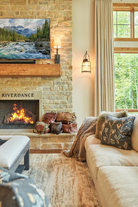 This rustic, neutral cottage living room features an inviting stone fireplace, beige sofa, gray ottoman, and metal lantern sconces. Neutral Cottage, Gray Ottoman, Grey Ottoman, Cottage Living Room, Sofa Gray, Black River, Cottage Living Rooms, Rustic Retreat, Beige Sofa