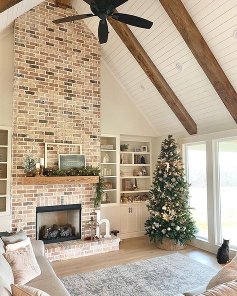 Floor to ceiling brick fireplace with wood mantel is connected to a white shiplap vaulted ceiling with wood beams. A black ceiling fan hangs over a gray area rug in front of the fireplace. Elk Over Fireplace Living Rooms, Vaulted Ceiling With Wood Beams, White Shiplap Ceiling, Stone Fireplace Floor To Ceiling, Fireplace With Shiplap, Ceiling With Wood, Red Brick Fireplace, Ceiling Beams Living Room, Planning 2024