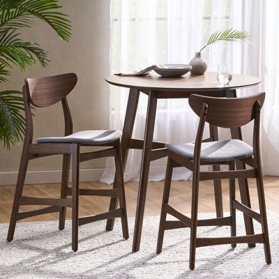 This 3-piece dining set makes itself the hub of your kitchen, breakfast nook, or dining room. Crafted from solid and engineered wood, this set features one dining fixed table and two dining chairs - it seats up to four people, so it's ideal for cozy meals. The circular table shows off splayed legs and crossed supports, while the side chairs sport curved backs and contoured seats. Fabric upholstery and a two-tone gray and walnut hue give this set a mid-century modern look that we love in any cont High Top Round Table, High Top Dining Table, Top Kitchen Table, Round Kitchen Table, High Top Tables, 3 Piece Dining Set, Round Dining Set, Solid Wood Dining Set, Table For Small Space