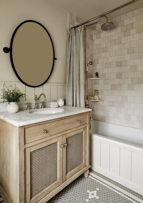 An oval bronze pivot mirror hangs over a beige cane washstand accented with a honed marble countertop finished with a polished nickel hook and spout faucet. Becca Interiors, Rustic Farmhouse Bathroom Ideas, Modern Farmhouse Bathroom Ideas, Timeless Bathroom Design, Bathroom Mirror Design, Farmhouse Bathroom Ideas, Bathroom Stand, Rustic Farmhouse Bathroom, Farmhouse Bathroom Design