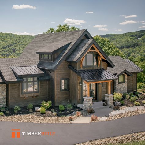 The back exterior half of a timber frame house. This house is finished in a dark green wood siding with stone accent pieces on the master bedroom. The timbers supporting the covered porch over the entryway are a natural color. This house is in forested hills and looks really fantastic. Timber Tech Deck Ideas, Small Covered Porch, Frame Design Ideas, Timber Frame Architecture, Modern Timber Frame Homes, Timber Frame Porch, Timber Frame Design, Entryway Porch, Timber Frame House