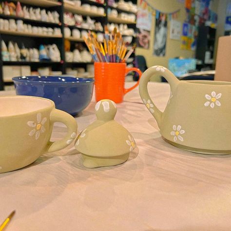 Sage green pottery tea set with minimalistic white flowers on a paper covered table. Includes tea pot, tea cup and life. Background is an art studio with painted pottery on shelves and paintbrushes Pottery Painting Ideas Green, Pottery Painting Green, Sage Green Pottery, Pottery Painting Date, Pottery Date, Aesthetic Pottery, Floral Tea Set, Date Idea, Cute Date Ideas