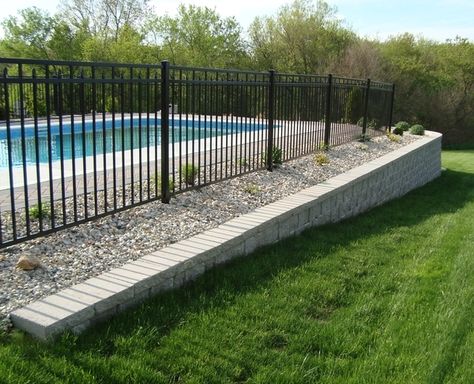 A retaining wall made of StoneWall Select block stabilizes the area around an in-ground pool. Sloped Pool, Retaining Wall Around Pool Ideas, Above Ground Pool Retaining Wall, Retaining Wall For Pool, Backyard Pool Fence, Above Ground Pool With Retaining Wall, Retaining Wall With Fence, Retaining Wall For Pool Sloped Backyard, Pool Fence On Retaining Wall