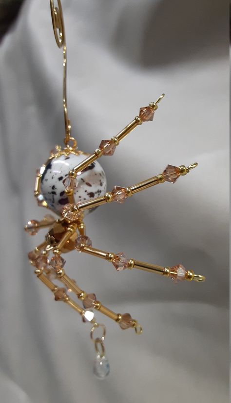 "This is a handmade beaded crystalline spider. The abdominal area is made from a mottled white and pearlescent ceramic bead and the head from a smaller metallic gold faceted bead. The legs are made form 21 ga. wire which are covered with small gold and Swarovski Glass crystal beads that can be carefully adjusted to almost any position. A gold decorative hook is attached to the back of the abdomen and can be used to hang the spider or be removed. The spider can be used as a Steampunk accessory on Diy Glass Jewelry, Diy Bead Spider, Christmas Spider Ornament Diy, Small Bead Crafts, Beaded Spider Tutorial, Bead Diy Crafts, Beaded Spiders How To Make, Bead Spider Web, Beaded Spider Web