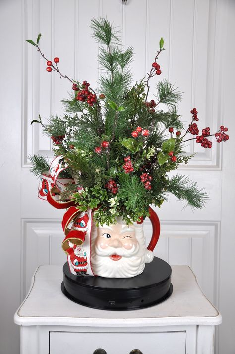 This  Winter Centerpiece will make you smile. It will also entertain the children. It is put together in a water picture made to look like the jolly old man who bring gifts.  I have added several types of iced greenery for texture and interest. There are red berries. I have added an adorable bow. This will be a cute addition to your Christmas decor. It can be displayed all winter. This arrangement measures approximately 24" high x 19" in diameter. These measurements are from tip to tip of the lo Christmas Decor Arrangements, Farm Table Christmas Centerpiece, Small Christmas Floral Arrangements Diy, Table Centerpieces For Christmas Party, Christmas Evergreen Centerpieces, Christmas Tabletop Decor Ideas, Simple Christmas Arrangements, Xmas Centerpiece Ideas Diy, Christmas Party Centerpieces Diy Cheap