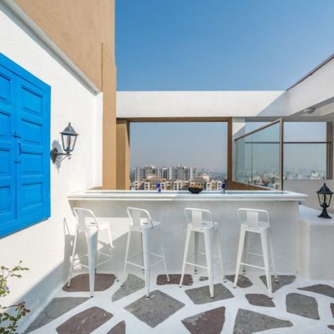 A raised wooden platform is reserved for meals or board games without disturbing the rest of the space. A vertical garden shields the duct area while radiating beauty through imperfections. “It helps to bring the outdoor inside and gives the monotonous flooring a break. It also feels very soothing and refreshing,” says Shah. A recycled blue window dresses up a plain wall while adding a dreamy note to the terrace. Inclined Studio, Theatre Style Seating, Santorini House, Penthouse Interior, Greek Decor, Terrace Floor, Door House, Mediterranean Interior, Mediterranean Style Home