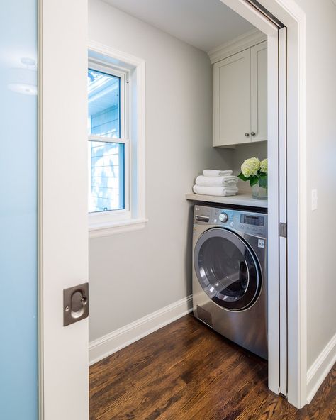 Pocket doors open to small mudroom boasting gray walls framing a window flanked by face to face washer and dryer situated under gray countertop doubling as folding station under shaker cabinets atop oak stained wood floors. Laundry Nook, Laundry Room Storage Shelves, Tiny Laundry Rooms, Laundry Room Doors, Grey Countertops, Laundry Room Cabinets, Laundry Closet, Small Laundry Rooms, 아파트 인테리어