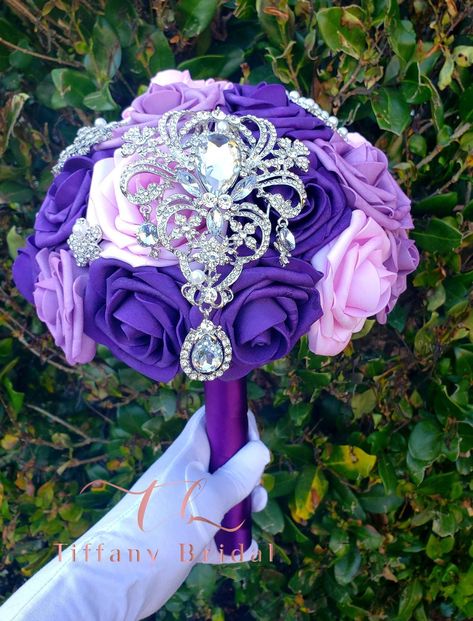 Description: Introducing our ultra-chic bridal bouquet of flowers designed with the style of jeweled brooches, glimmering, and sparkling in the light. This brooch bouquet is sure to attract everyone's attention! You can order your wedding bouquet can be ordered online directly on our site. The custom, handcrafted bouquet is glamorous in luscious soft touch roses. Carefully arranged diamond-inspired rhinestone brooches add glitz to the romantic design. When you're planning a luxurious wedding wit Mother Of The Bride Bouquet, Purple Brooch Bouquet, Rose Gold Bouquet, Bouquet Keepsake, Purple Brooch, Gorgeous Wedding Dress Princesses, Toss Bouquet, Gold Bouquet, Bouquet Bridesmaid