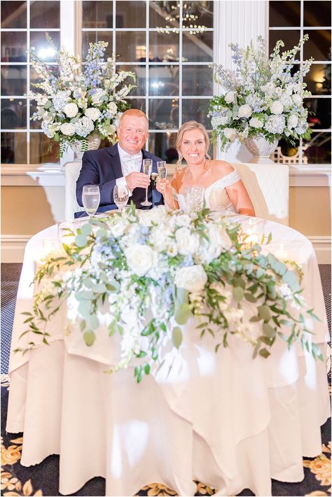 bride and groom sit at sweetheart table with white and blue floral details | Elegant costal Bonnet Island Estate Wedding with shades of blue details photographed by LBI wedding photographer Idalia Photography. Sweetheart Table Wedding Blue, Dusty Blue Sweetheart Table, Blue Wedding Ceremony, Blue And White Sweetheart Table, White Wedding Flowers Hint Of Blue, Blue Hydrangea Wedding Table Decor, Sweetheart Table Florals, Shades Of Blue Wedding, Blue Hydrangea Wedding Centerpieces Floral Arrangements