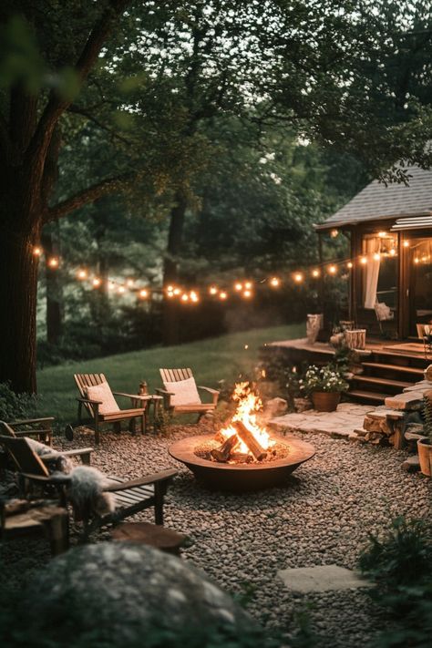 Cozy outdoor fire pit area with string lights, surrounded by wooden chairs and lush greenery. Fire Pit With Rocks Natural Stones, Fire Outside Ideas, Rustic Farmhouse Backyard, Fire Pit Beach House, Outdoor Circle Fire Pit, Modern Backyard Fire Pit Ideas, Patio Area With Fire Pit, Outdoor Fire Pit Lights, Home With Backyard