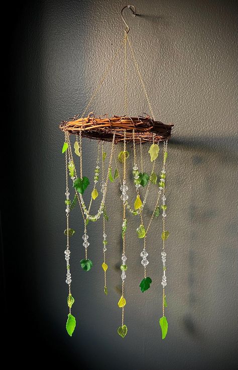 Round cottage core themed sun-catcher.  6'' round width; 20.5'' total length This decorative round sun-catcher is made with a grapevine wreath, gold chain, plastic leaves, and crystal beads. Nature Indoors Decor, Cottage Core Bedroom Decor Diy, Diy Light Catcher, Cottage Core Decor Diy, Cottage Core Crafts Diy, Cottage Core Door, Garden Theme Room, Beaded Suncatcher Diy, Sun Catchers For Kids