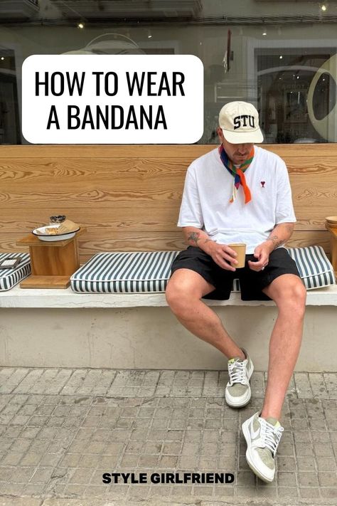 image of a man sitting on a bench wearing a white baseball cap, white t-shirt, orange patterned bandana around his neck, dark shorts, and Nike sneakers. Text on-screen reads: how to wear a bandana How To Tie A Neckerchief Men, Men Neckerchief Outfit, Men Summer Scarf, Bandana Scarf Outfit Men, Neck Bandana Outfit Men, Mens Bandana Style, Neckerchief Outfit Men, Men Bandana Style, Neck Bandana Outfit