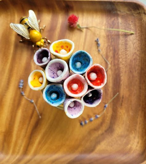 Top view of Blue, red, yellow, dark and light purple ceramic cone flower bouquet. Each flower has a white edge detail. On a wood background with an enameled bee, dried lavender and clover. The flowers are bee cup stakes for in the garden to offer a safe hydration station for pollinators. Bird Bath Pottery, Pottery Bird Bath, Fun Pottery, Ceramic Bird Bath, Bee Cup, Clay Lesson, Heat Waves, Diy Ceramic, Everyday Art