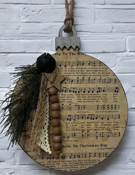 Wood ornament door or wall hanger.  This ornament is covered in Christmas music paper and embellished with Christmas greenery, neutral colored ribbons, wood beads, a wooden star and a black bell. It is distressed for a rustic farmhouse look.  Jute hanger attached.  Measures approximately 9" tall x 7.5" wide x 1/4" thick. Hanger Christmas Decoration, Mitten Door Hanger, Wood Ornament Door Hanger, Wood Heart Ornaments, Christmas Ornaments On Wood Slices, Christmas Wood Crafts To Sell Rustic, Circle Door Hangers Wooden Diy, Christmas Round Wood Signs, Spool Christmas Ornaments