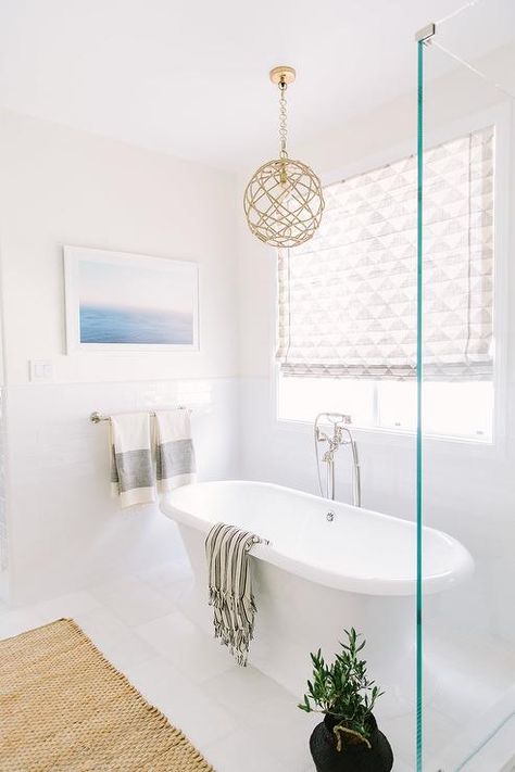 A rope pendant light hangs over a roll top freestanding bathtub fitted with a floor mount polished nickel tub filler and positioned beneath a picture window covered in a light gray and white geometric print roman shade. Pendant Light Over Bathtub, Light Over Bathtub, Bathroom Chandelier Lighting, Bathtub Light, Bathroom Chandelier, All White Bathroom, Rope Pendant Light, Transitional Bedroom, Bathroom Pendant