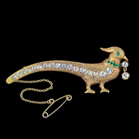 A wonderful antique Edwardian pheasant brooch lined with seventeen sparkling old mine-cut diamonds that graduate from the head all the way down his long tail feathers. They have SI 1/2 clarity – H/I colour and range from 0.06 – 0.20ct (approx. 2ct total).] The head of the bird is also set with an emerald eye, a collar of glistening emerald-green pastes and a double diamond dropper hanging from his beak. It's modelled in solid 18ct gold with feather texturing etched across the front. It's a ... Brooch Diamond, Feather Texture, Emerald Eyes, Double Diamond, Antique Brooches, Tail Feathers, Gold Jewellery Design Necklaces, Cushion Cut Diamonds, Beautiful Doors