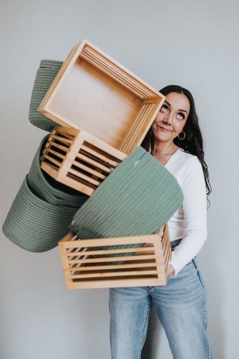 A woman with dark hair wearing a white long-sleeve shirt and blue jeans is holding a stack of balancing green fabric baskets and wooden crates while look up and to the right. Staging Branding Photos, Professional Home Organizer, Organizer Branding Shoot, Personal Organizer Ideas, Professional Organizer Photoshoot, Linen Photoshoot, Professional Organizer Business, Photography Organizations, Branding Headshots