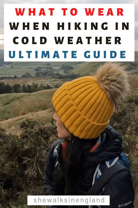 What to wear when hiking in cold weather ultimate guide, written by she walks in England. There is a photo of Zoe wearing a yellow wool bobble hat, with a back drop of countryside hills and fields. Cold Weather Hiking Gear, Hiking In Cold Weather Outfit, Cold Hike Outfit, Hiking Cold Weather Outfit, What To Wear For Hiking, Cold Weather Hiking Outfit, Cold Hiking Outfit, Warm Hiking Outfit, Winter Outdoor Outfits