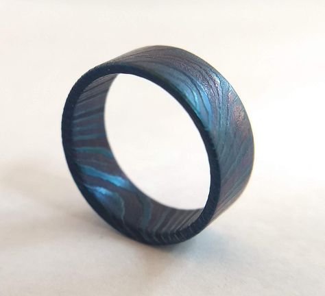 This hand-made solid steel ring is milled from a single piece of damascus steel. The entire ring is acid etched to give a unique 3-D texture, sanded and polished, and finally flame treated to permanently color the surface of this ring with beautiful blues, greens, and maroons. The inside of the ring is sanded and contoured to give a comfort fit and the entire ring is rubbed with steel wool to give an all around smooth feel This piece is a unique, one of a kind ring that is sure to be a conversat Timascus Ring, Gold Vintage Rings, Damascus Ring For Women, Damascus Jewelry, Men’s Wedding Bands Damascus Steel, Aquamarine Engagement Ring Vintage, His And Hers Rings, Damascus Ring, Damascus Steel Ring