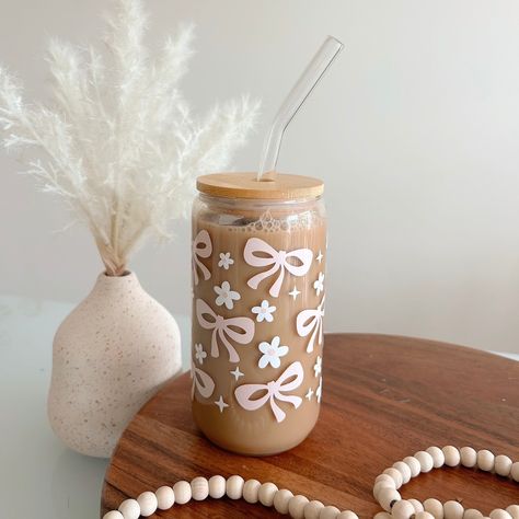 Bows and Daisys Tumbler with Straw - 16oz Celebrate your love for coffee with this glass tumbler! This 16oz tumbler is perfect for every caffeine lover out there. This glass tumbler comes with a natural wooden lid and a sleek, reusable glass straw, making it both a chic and sustainable choice for your drinkware collection. Perfect for iced coffee, smoothies, or any cold beverage, this tumbler is a great companion for busy days, whether at home or on the go. It also makes a thoughtful gift for all the special people in your life! Product Details: *Capacity: 16oz *Material: Glass with a wooden lid *Includes: Reusable glass straw *Design: Daisys and bows *Ideal for cold beverages *Eco-friendly and reusable Care Instructions: *Hand wash only *Do not microwave  *Do not put in dishwasher Sip in Cute Coffee Glass Cups, Iced Coffee To Go Cup, Cute Glass Coffee Cups, Glass Tumbler With Straw, Iced Coffee Cups, Painting Glass Jars, Straw Design, Trendy Water Bottles, Cute Coffee Cups