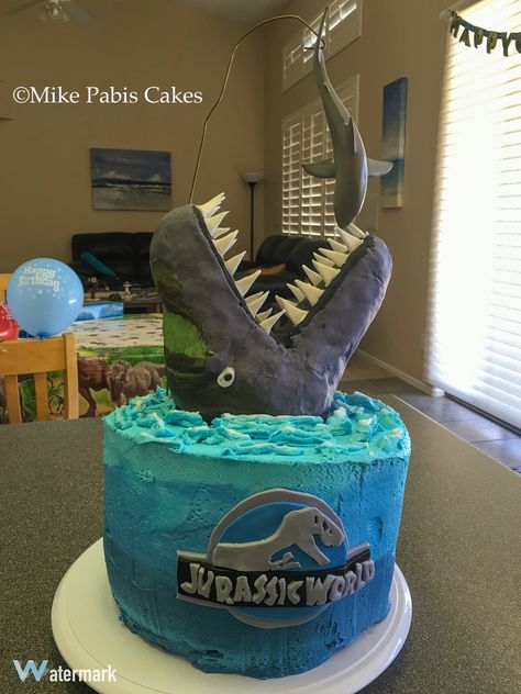 Jurassic World Mosasaur cake featuring the dinosaur jumping out of the water to eat the great white shark. Features four layers of chocolate chip cake with ganache and cookie dough in between. Stands over 18" high and and weighs about 20 pounds Shark Dinosaur Cake, Shark And Dinosaur Cake, Mosasaurus Cake, Shark Birthday Cakes, Jurassic Park Birthday, Thomas Birthday, Park Birthday, Dino Birthday Party, Monster Cake