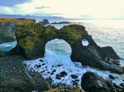 Gatklettur Arch, Iceland.Located near Arnarstapi, at Snæfellsnes Peninsula, West Iceland.  Gatklettur (“Hole cliff”) is a cliff with a circular arch. Rock Arch shows how distinctive wave action has eroded the rocks into arches and beautiful swirled patterns. There is great birdlife around the cliffs and pretty flora surrounding the area. Circular Arch, Rock Arch, Midnight Summer, West Iceland, Snaefellsnes Peninsula, Beach Rocks, Holiday Destinations, Fall 2024, Summer Sun