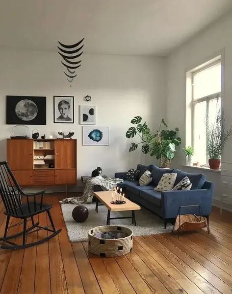 a mid century modern living room with a navy sofa, a black rocker, potted plants, a stylish gallery wall and some cat furniture Living Room Decor Blue Sofa, Mid Century Modern Living Room Decor, Blue Sofa Living, Blue Sofas Living Room, Blue Living Room Decor, Mid Century Living Room, Mid Century Modern Living, Mid Century Modern Living Room, Wooden Floors