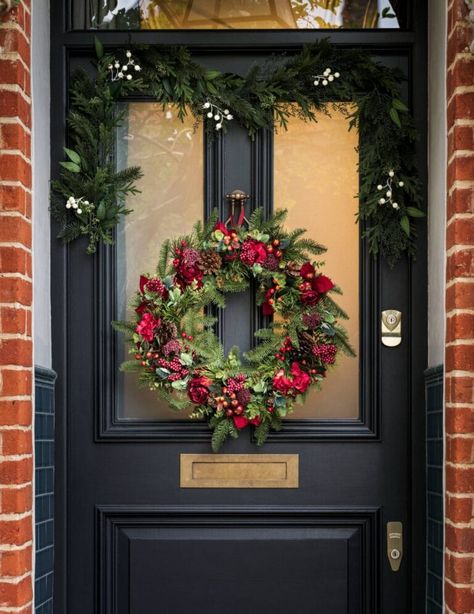 Wow, check out this festive front door! It's got a beautiful wreath with red berries and greenery, and there's even a garland draped across the top. It's the perfect way to welcome guests during the holiday season! Festive Dining Table, 4 Seater Dining Table, Bell Decorations, Real Christmas Tree, Star Garland, Decorating Styles, Metal Lanterns, Christmas Placemats, Metal Stars