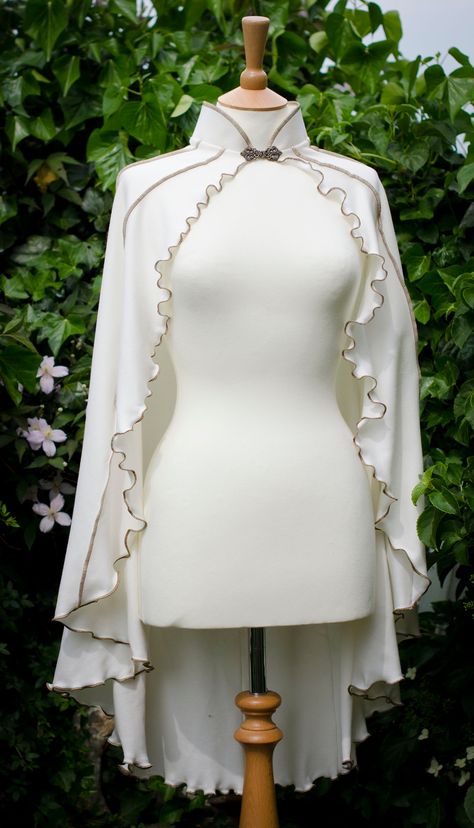 ~ White Driud Lily Capelet ~ Made to Measure ~ Original made in White material with Antique Gold thread & brass clasp ~  The Druid Lily Capelet is made from lovely stretchy cotton jersey with vertical striped detail, lettuce-edging & mandarin collar. It has a metal clasp closure at the throat, the clasps that I currently offer are a different style to those photographed on the cape. You can see the new style and colours in the last image. Perfect for Fanciful Faeries, Gothic Goddesses & Pixchiev White Elf Costume, White Robes Fantasy Aesthetic, Cape Aesthetic, Cloak Designs, White Gold Outfit, White Ballet Dress, White Dress Design, Dress Coverup Ideas, Elven Cape