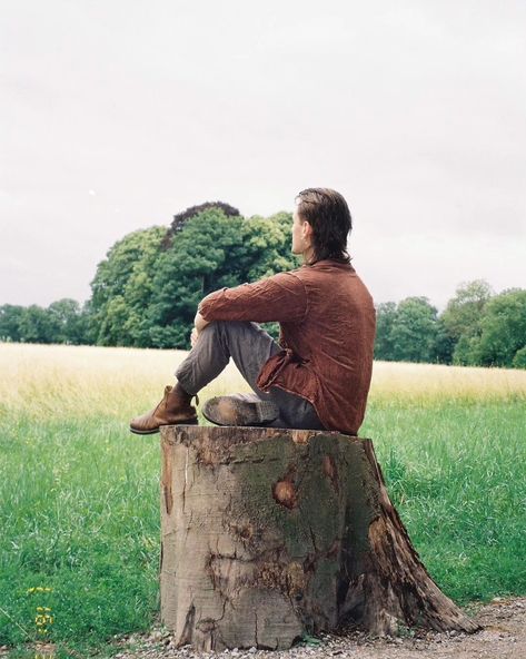 Person sitting on a log in a forest. They're wearing boots, green linen pants, and a brown blouse. They have a mullet and earrings. Person Sitting Down Looking Up, Sitting On Ground Reference Drawing, Sitting On A Log Reference, Person Sitting Looking Up, Sitting Behind Reference, Person Sitting On Ledge, Person Sitting Back View, Person Sitting From Behind, Person Turning Around Reference