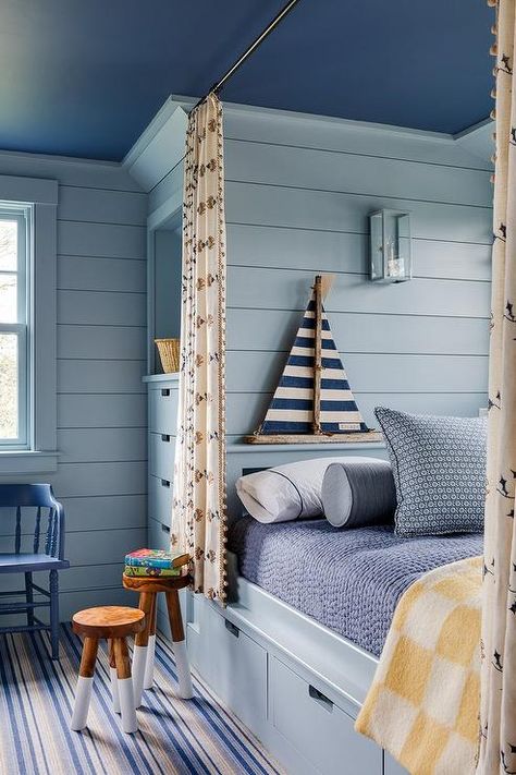 Cottage style boy's bedroom features a blue built in twin bed with dark blue painted ceiling, blue shiplap trim, chintz pom pom curtains and a blue stripe rug with wooden stools. Nautical Theme Bedroom, Coastal Cottage Bedroom, Boys Bedroom Ideas, Boys Room Design, Nautical Bedroom, New England Home, Home Design Interior, Blue Ceilings, Interior Home Design