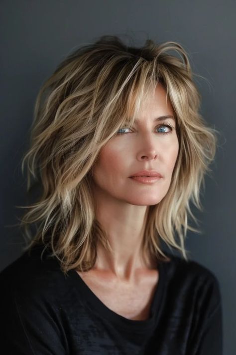 A woman with tousled short blonde hair and blue eyes, gazing to the side, against a grey background. Long Bob With Choppy Layers, Shag Hairstyles Low Maintenance, Choppy Layered Bob Hairstyles Medium, Shaggy Bangs Fine Hair, Shaggy Layered Haircuts Medium Fine Hair, Edgy Textured Haircuts, Shag No Bangs Hairstyles Medium, Medium Shag With Bangs Fine Hair, Choppy Lob Fine Hair