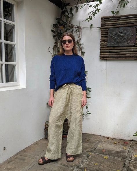 A woman stands on a patio. She wears green striped linen trousers, blue jumper, sunglasses and Birkenstock Arizona sandals. Arizona Birkenstock Outfit, Birkenstock Arizona Outfit, Arizona Birkenstock, Flight Outfit, Jumper Shorts, Birkenstock Outfit, Birkenstock Sandals Arizona, Blue Jumper, Spring Outfit Ideas