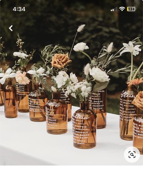 Amber Glass Vase With Flowers, Amber Glass Bottles Wedding, Glass Bottle Seating Chart Wedding, Bourbon Wedding Centerpieces, Amber Glasses Wedding Table, Amber Jar Centerpiece, Brown Glass Bottles Wedding, Glass Bottle Seating Chart, Brown Glass Wedding Centerpieces